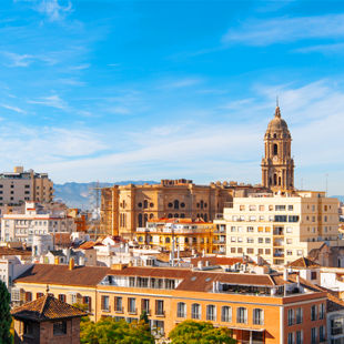 Uitzicht op Málaga met dichtbebouwde stad, haven aan de kust en bergen op de achtergrond onder een heldere blauwe lucht.